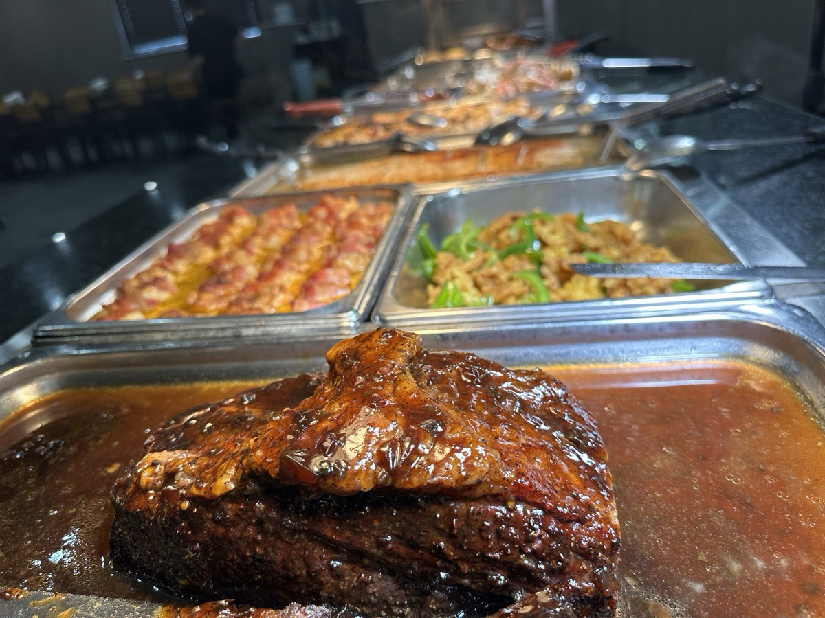 A braised meat dish in the foreground with the hot line behind