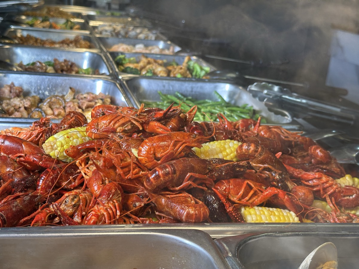 A steaming tray of seasoned crawfish with corn on the cob on the hot line