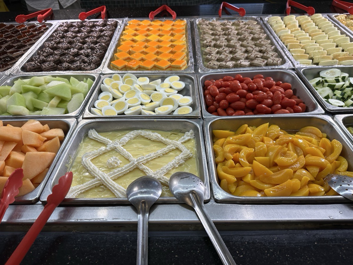 Buffet trays of desserts, melon, eggs, cherry tomatoes and sliced peaches