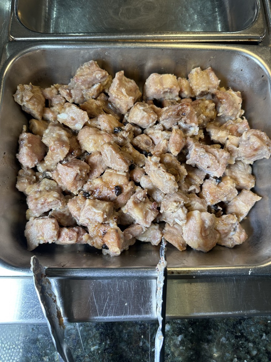 A serving tray of browned diced cooked meat on the hot line