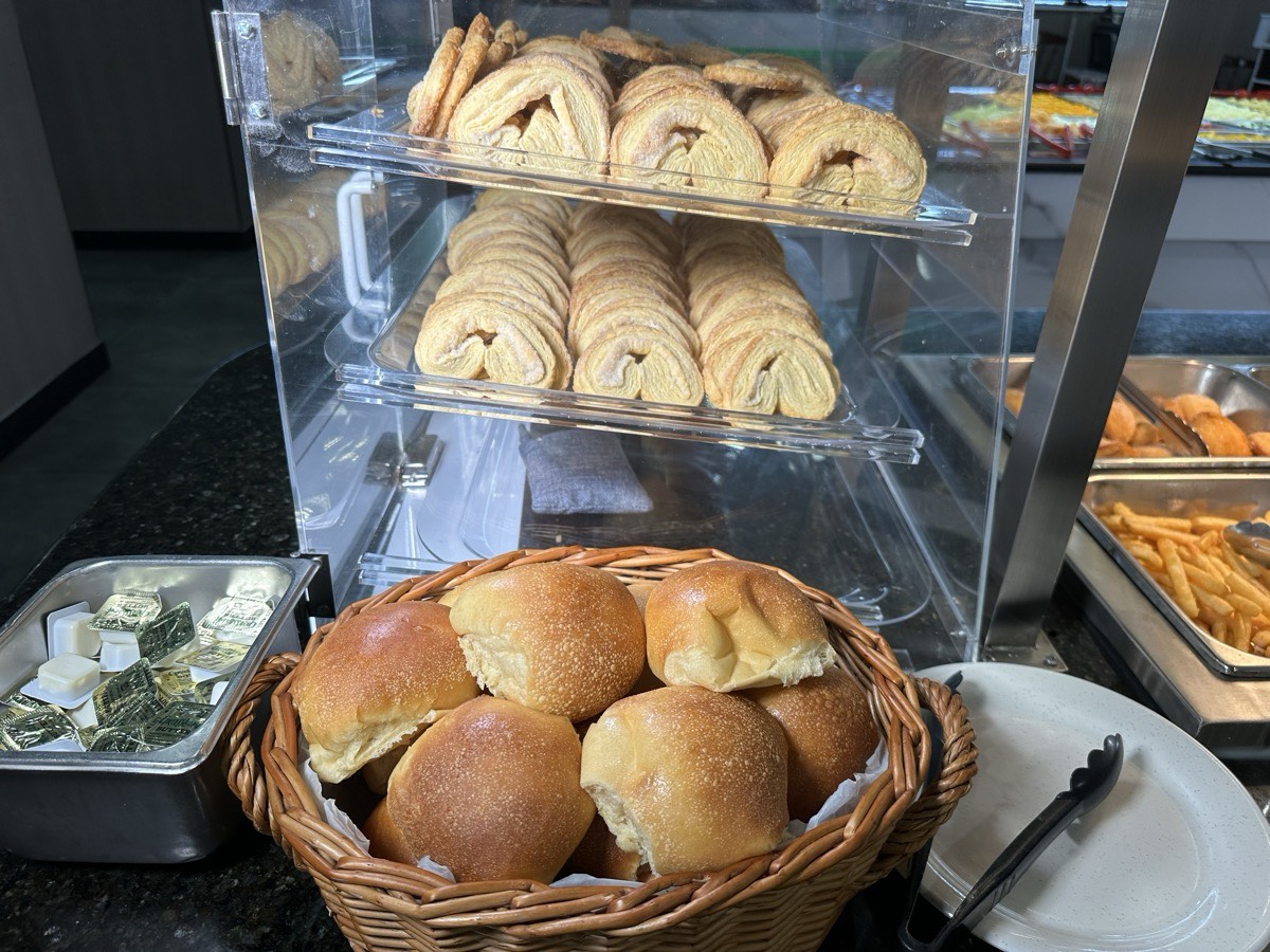 Pastries in a display case beside a basket of fresh dinner rolls and butter
