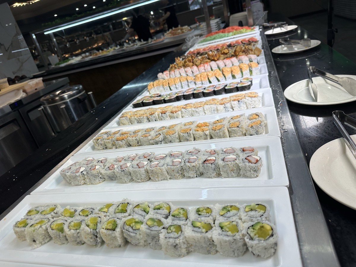 Sushi rolls set out along the buffet line beside stacks of plates