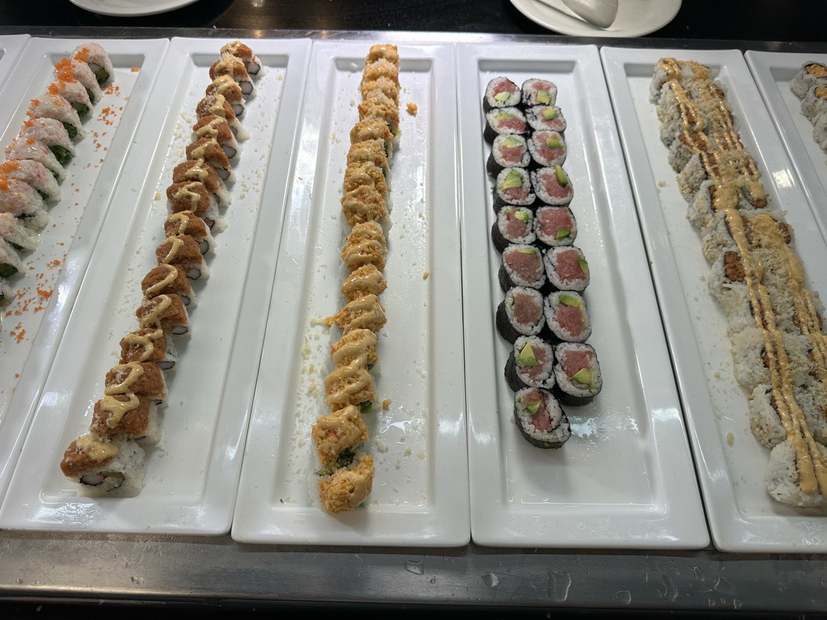 Four long platters of assorted sushi rolls on the buffet
