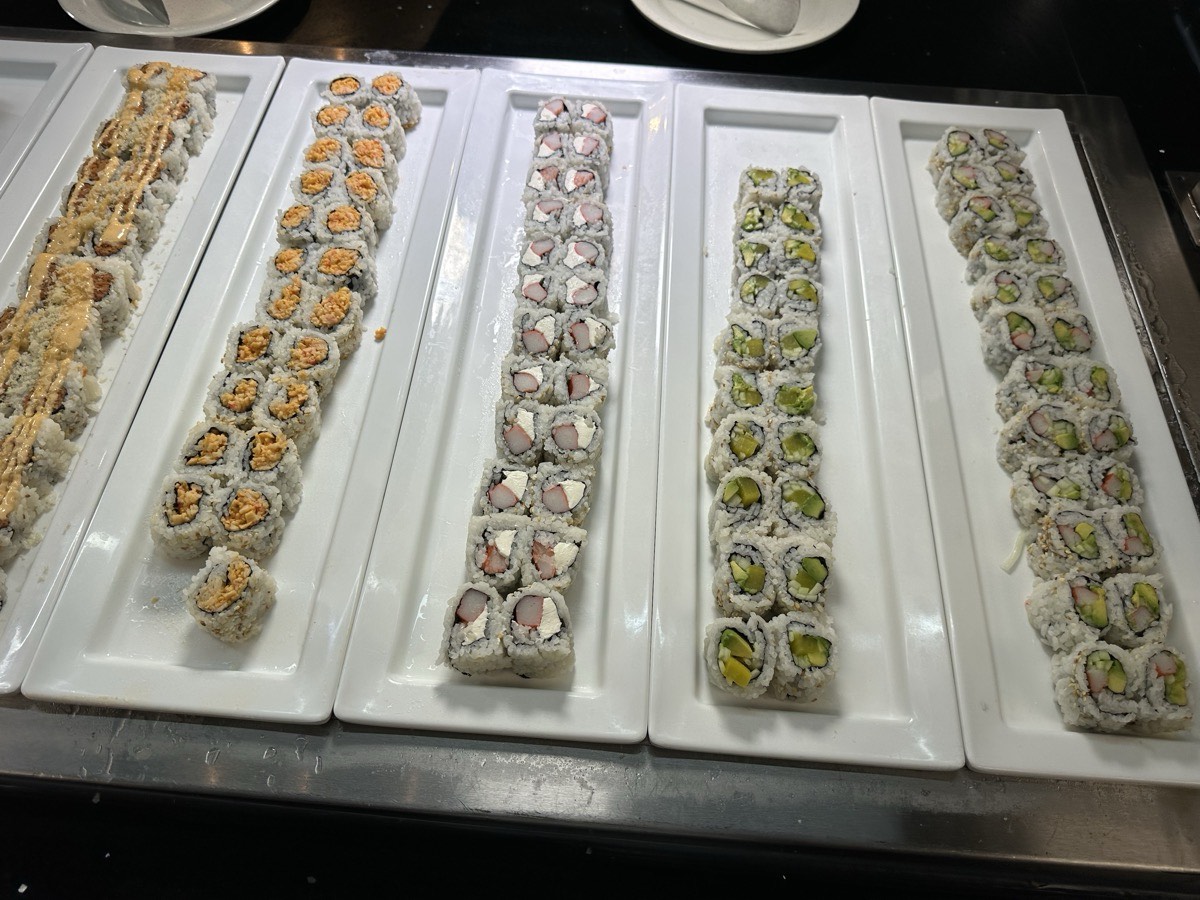 Trays of sushi rolls arranged in rows on the buffet line